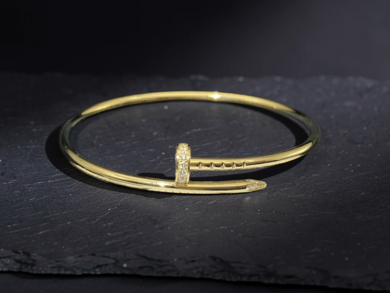 Dasselbe goldene Armband auf dunklem Schiefer in warmem, gedämpftem Licht, in PhotoFig bearbeitet
