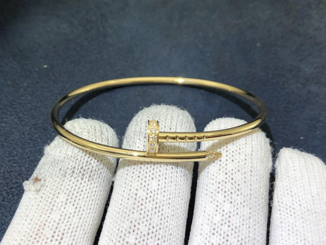 Goldenes Armband in Nagelform, mit einem weißen Handschuh vor dunklem Hintergrund gehalten