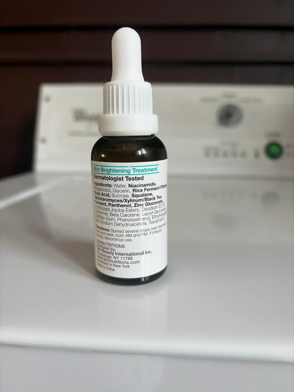 Amber serum bottle with a white dropper and printed label, photographed on an appliance